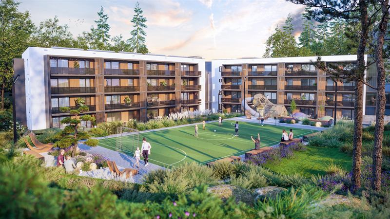 Areál aparthotelu v létě, travnaté hřiště, dětské prolézačky a lidé před domem
