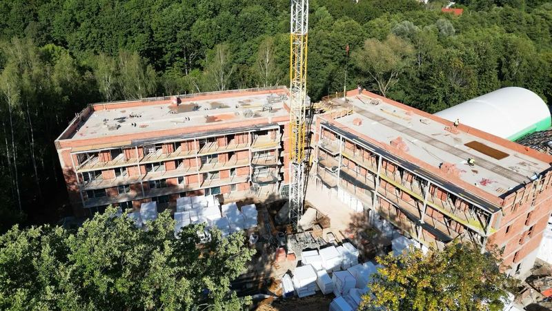 Letecký snímek stavby aparthotelu v září 2026, obě křídla v hrubé stavbě s jeřábem